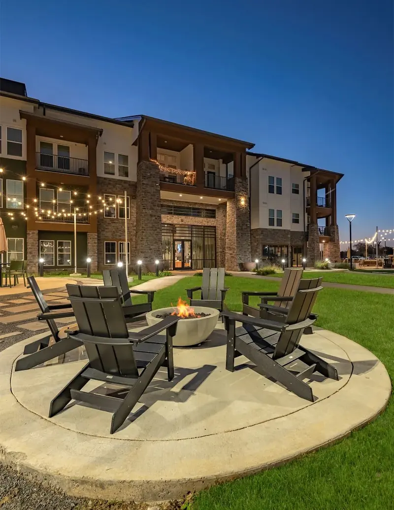 Courtyard fire pit with Adirondack chairs under string lights at dusk